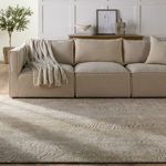 Living room scene with beige sofa, pouf, and decorative accents on wall behind sofa