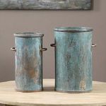 Set of two tall cylindrical iron containers with a tarnished copper finish and side handles on a wooden table