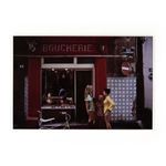 Vintage street scene showing three women and a child conversing outside a red boucherie storefront with a bicycle