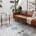 Skye Silver/Grey rug styled under brown leather sofa and white chair in bright living room corner