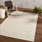 Soft tribal rug laid on wooden deck paired with black woven chair and white side table