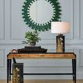 Box placed on wood desk beneath green-framed round mirror as part of styled vignette with lamp and plant