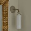Side angle of sconce mounted beside woven framed mirror with neutral wall background