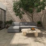 Outdoor setting with gray toned sectional on tiled patio under leafy tree with round marble coffee table