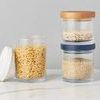 Set of three clear glass canisters with different lids and filled with dry foods on marble surface