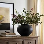 Black terracotta Civita Vase styled with large leafy branches on wooden sideboard against light wall