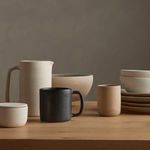 Salt jar with other ceramic kitchen accessories on wooden surface against gray wall