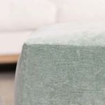 Close-up angled view of pouf’s soft velvet top surface with white sofa background