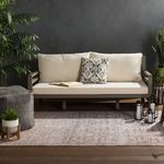 Straight-on view of rug under beige sofa with a dark knitted pouf and potted plants beside