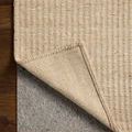 Rug corner lifted to reveal underside and the contrasting gray rug pad beneath