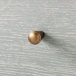 Close-up of round gold metal drawer knob set against gray cerused oak wood grain