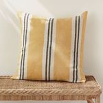 Front view of yellow striped pillow resting on wicker bench with sunlight shadows