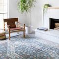 Clara Blue rug styled in a bright living room with leather chair, potted plant, and white fireplace