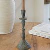Single Bristol candlestick with beige taper candle placed on wooden table beside white textured vase and books