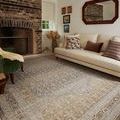 Rug in living room setting with beige sofa, floral pillows, green armchair, and rustic brick fireplace