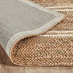 Back side of rug partially flipped to reveal tightly woven grey backing and edge stitching