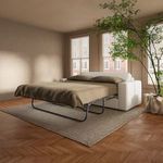 Side angle of Kiran sleeper sofa bed open with brown bedding in light-filled room