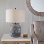 Neolithic Blue Gray Table Lamp on a light wood side table with beige armchair and round wall mirror in background