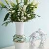 Console table displaying tall white vase with colorful mosaic band and porcelain bird figurines