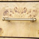 Close-up of antique brass drawer pull mounted on burl wood grain drawer front