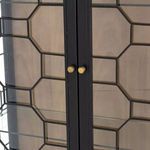 Close-up of brass door knobs centered on black honeycomb metal-framed glass cabinet doors.