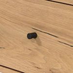 Close-up of single black metal knob handle on oak drawer showing wood grain detail