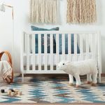 Chevron rug placed under crib with white slats, plush lamb toy, and blue accent pillows