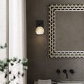 Bath wall sconce installed on textured gray wall next to a decorative framed mirror above white marble sink