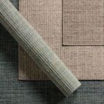 Overhead view of rolled rug over two solid color rugs in muted beige and beige-gray tones