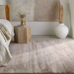 Tan/cream abstract rug placed in bedroom setting with wooden side table, large white vase, and neutral bedding