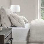 Side view of gray linen duvet on bed with matching textured pillows and bedside lamp in neutral room