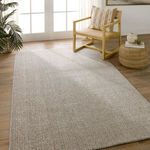 Rug placed in a sunlit room beside woven chair and ottoman on wood flooring