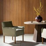 Dining room setting with khaki armchair beside round stone-top table and wood-paneled wall