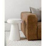 Book accent table styled beside tan leather sofa on a chunky knit white rug