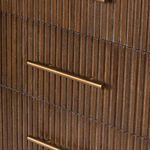 Close-up of polished brass handle mounted on vertical reeded wood drawer front.