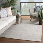 Rug styled on outdoor patio with gray wicker furniture, colorful pillows, and greenery around