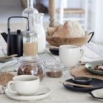 Pacifica mugs styled on a dining table with jars, milk, bread, and black dishware in cozy kitchen setting