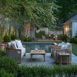 Outdoor patio setting with Avalon Teak Swivel Lounge chairs arranged by pool with evening lighting