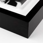 Close-up of black wooden frame corner and white mat surrounding black and white photo