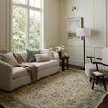 Rug styled in a bright living room under sofa and armchair with neutral walls and floors