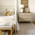 Rug styled in bedroom under a cream-colored bed and beige dresser with lamp and decor