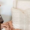 Pillow placed on cream armchair next to pink textured throw blanket