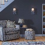 navy polka dot wallpaper applied on angled wall in room with floral armchair and matching ottoman