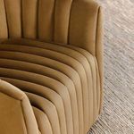 Detailed close-up of seat and inner armrest tufting on bronze swivel accent chair on woven rug