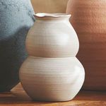 Chyrssa Vase with warmer tone placed on wood surface with textured black and terracotta vases in background