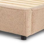 Close-up of camel sheepskin upholstery on corner of low-profile bed frame above short black legs