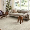 Ivory rug styled in bright living room under sofa and wooden stool with pillows and a floor plant