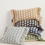 stack of pillows in five color variations including blue, black, green, gray, and rust with geometric pattern and tassels