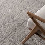 Close-up of rug next to wooden chair leg showing fine weave detail and muted color palette