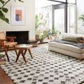 Yeshaia rug in a sunlit room with white walls, modern sofa, wooden chairs, and large windows